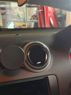 A close-up of a circular car air vent cover installed on a dark gray dashboard, with a matching round black cover on the left. The vent has a textured silver outer ring and a small white 'JYP' logo at the bottom.